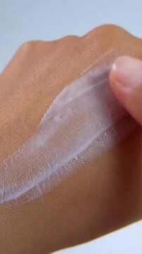 Gently applying moisturizing cream to back of hand. Top close up view. Vertical video for UV self care concept, daily hydration and skin protection.