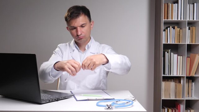 Male doctor in a white coat showing professional frustration and disappointment, tearing up a document in his office, symbolizing medical error, failure, and stress in healthcare