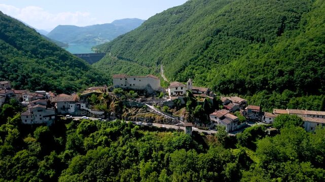 Lago di Turano Posticciola medieval borgo drone lateral flight over hilltop town Italy. Cinematic aerial tracking shot over ancient stone houses toward Turano dam and turquoise lake in green valley.  