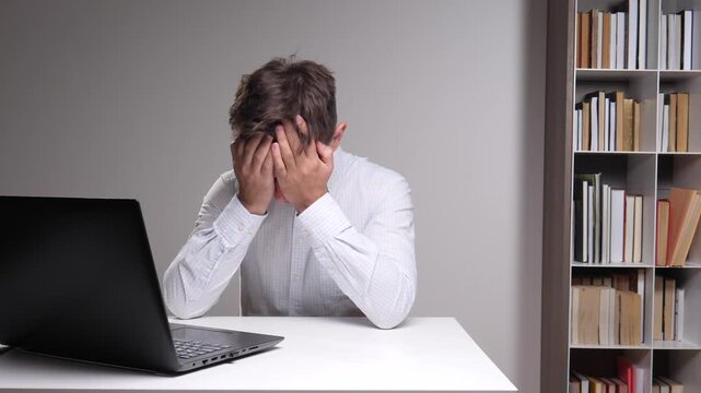 Man feeling stressed and frustrated, covering his face with his hands while sitting at a desk with a laptop, experiencing burnout and exhaustion from work pressure