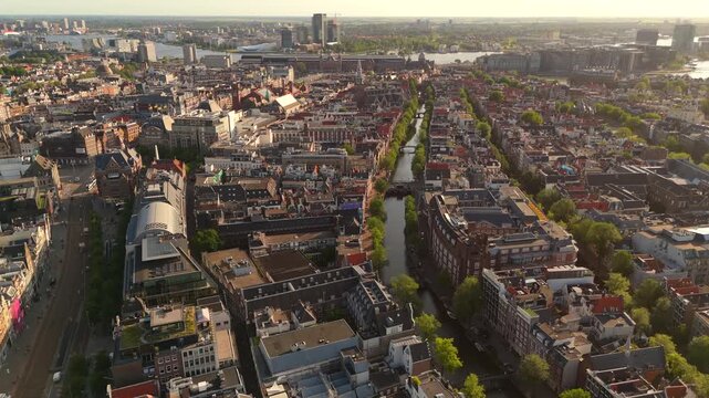 Drone flies forward above Amsterdam centered over a narrow tree lined canal with the IJ waterway and city on the horizon
