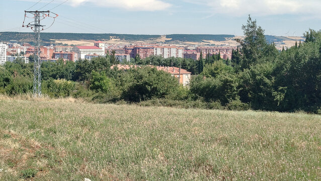 Vista de una ciudad con edificios detr&aacute;s de un campo verde con &aacute;rboles y una torre de alta tensi&oacute;n en Burgos, Espa&ntilde;a