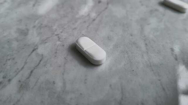 Extreme closeup of medicine pills or tablets spill and falling down on white table by accident. Antibiotic, antidepressant or painkiller drug medication abuse, addiction and misuse overdose concept.