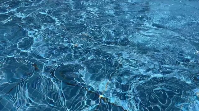Crystal clear blue pool water with sunny ripples and light reflections in a luxury resort setting perfect for summer vacation and tropical wellness concepts
