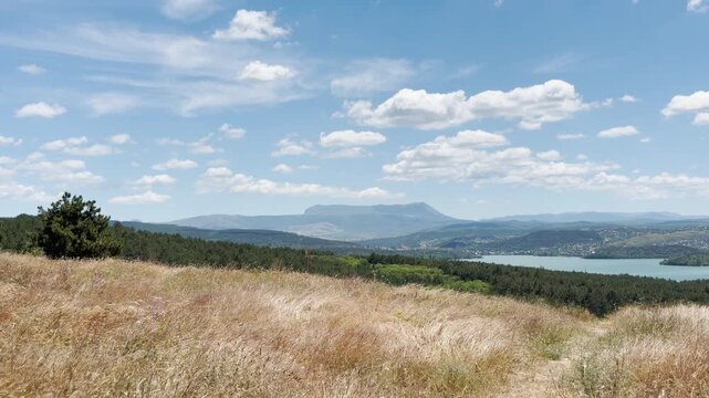 Majestic mountains stand peacefully on the horizon in Simferopol, Crimea. Golden grass waves under a bright, joyful sky near a calm blue lake.