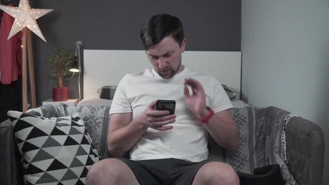 Man rubbing painful neck due to severe muscle tension before using cervical collar support, sitting on couch after prolonged smartphone strain. Putting on cervical orthosis brace, neck immobilization 