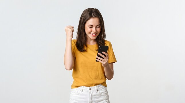 Portrait of a satisfied young woman holding mobile phone and celebrating isolated over white background
