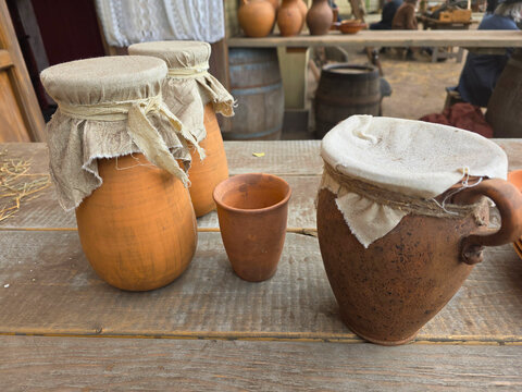 Traditional handmade clay jugs, earthenware pottery and ceramic cup displayed on a rustic wooden table in a historical village setting. Authentic antique ceramic vessels with natural textures