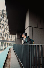Fototapeta premium Modern Urban Explorer: Man with Backpack Looking Out from City Balcony on a Cloudy Day