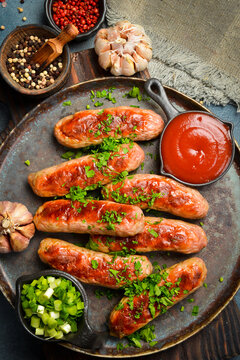 Grilled pork sausages with parsley, sauce and garlic. On a stone plate. Close-up.