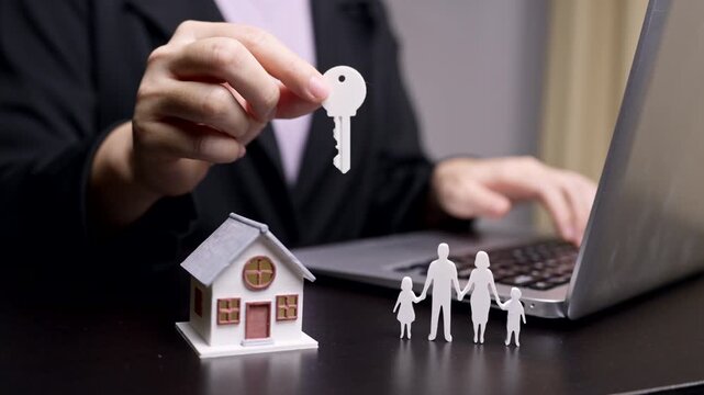 Real estate agent working on laptop with house model and family paper cutout, Home loan and property insurance concept.
