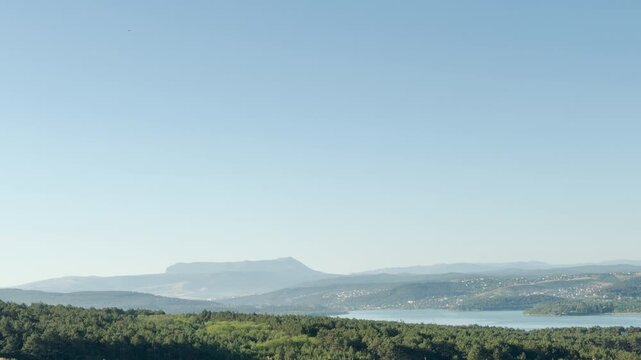 Majestic Mount Chatyr-Dag rises peacefully over a serene lake and lush green forest in Simferopol, Crimea. The calm landscape evokes a deep sense of tranquility and awe.