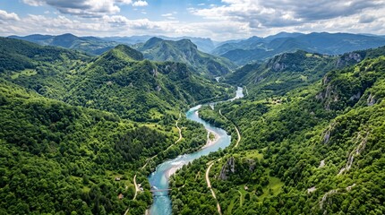 Aerial view of a winding alpine river flowing through a lush green valley surrounded by majestic snow capped mountain peaks under a bright summer sky © Waqasahmed