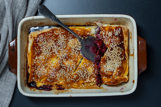 Homemade berry pie with sesame seeds in baking dish. Freshly baked golden cherry pie sprinkled with sesame seeds in ceramic baking pan with vintage spatula representing delicious homemade dessert