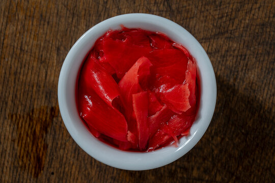Pickled pink ginger slices, closeup. Top view of marinated pink ginger gari in small white ceramic bowl on rustic wooden table background representing traditional Japanese cuisine and sushi condiment