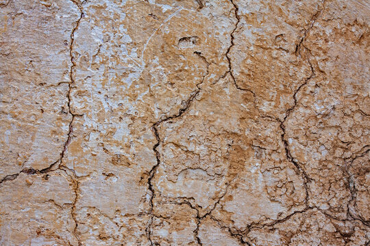 Cracked clay wall texture with rough weathered surface, closeup. Old weathered terracotta clay wall with deep cracks and scratches representing rustic background or ancient architecture concept