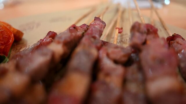 Grilled meat skewers served on wooden platter with roasted tomatoes in authentic italian restaurant style.