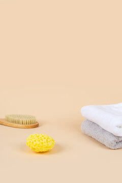 Minimalist spa and beauty product mockup background with copy space. Wooden body brush, yellow sea sponge, and stacked towels on warm beige background for cosmetic presentation.