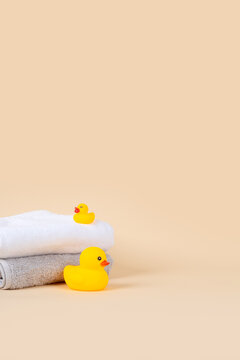 Baby bath product mockup background with vertical copy space. Cute yellow rubber ducks and stacked soft towels on warm beige background for newborn skincare presentation.