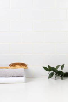 Minimalist bathroom product mockup with white subway tile background. Wooden tray with green leaf in glass and stacked towels with hairbrush for cosmetic display.