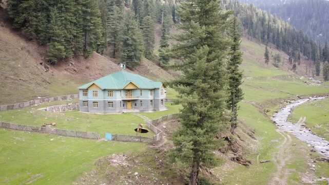 Aerial view of an isolated off-grid home surrounded by pine forests and a mountain river.