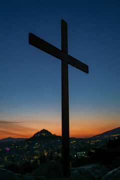 A silhouette of a cross on the Areopagus overlooking Athens, Greece at sunrise. Warm dawn tones frame the city skyline and distant hills, creating a powerful blend of faith, and history.