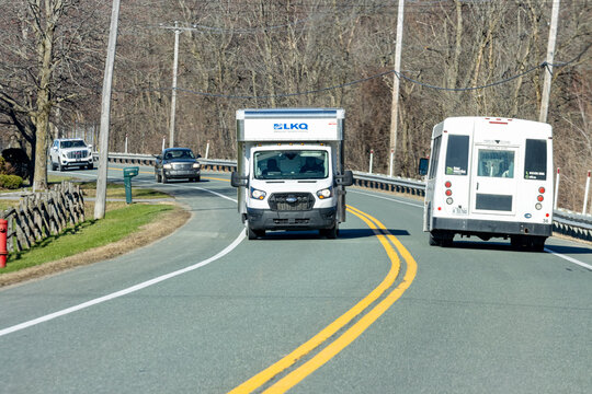 Quebec, Canada, 24 April 2026 : White LKQ box truck and a public transit bus drive on a winding road with bare trees.
