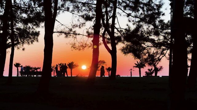 Seaside Boulevard at sunset. View of embankment of the resort town at evening. Silhouette people walking along the boulevard and ride electric scooter along the bike path. Backlight effect