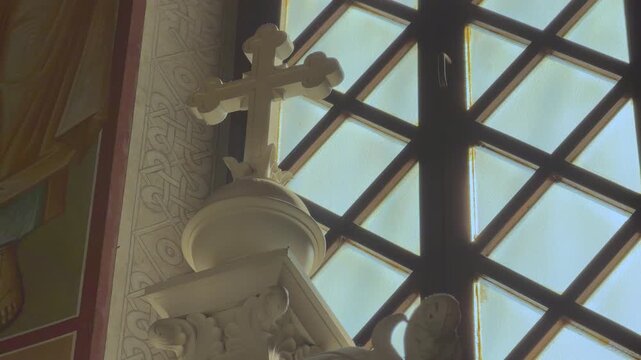 An ornate white sculpted cross and decorative carving inside an Orthodox church glowing softly beside a latticed bright window