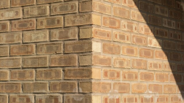 Brick wall displays a sharp corner meeting point where light and shadow create a high contrast triangular shape.