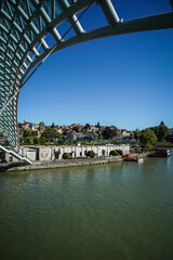 Modern Bridge of Peace arching over the Kura River, with historic Tbilisi cityscape in Georgia. © Greggory Zzyzx