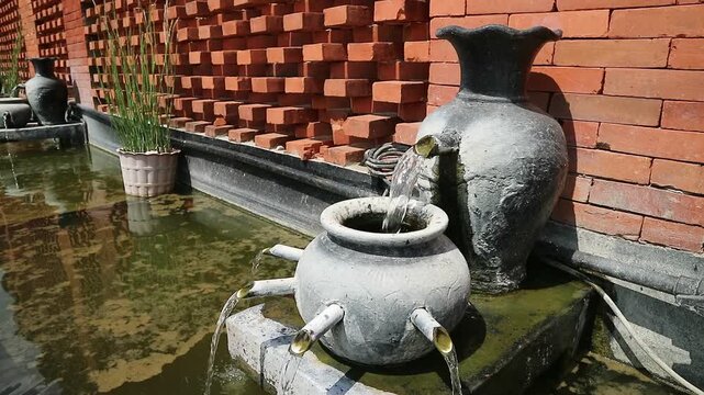 Water Flowing from Clay Pot in Outdoor Pond with Red Brick Wall