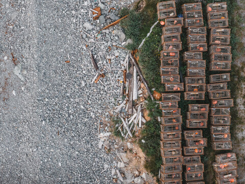Aerial view of stacked crab pots resting on a rocky shoreline with driftwood and sparse vegetation in Unalaska, Alaska, United States.