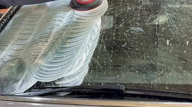 An employee of the detailing studio polishes the windshield of a car from chips, scratches using polishing machine. Detailing, polishing of the car. Car detailing - working with an orbital polishing. 