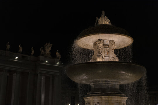 Illuminated Baroque fountain and the Bernini colonnade at night in St Peter's Square, Vatican