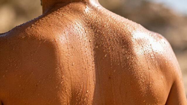 Close-up of sweat beading and dripping down a person bare back under harsh outdoor sunlight, skin glistening with perspiration. Heat stress and dehydration concept.