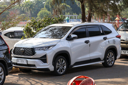 A white Toyota Innova Zenix parked in an outdoor parking area with trees in the background.