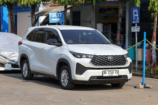 A white Toyota Innova Zenix parked in an outdoor parking area with trees in the background.