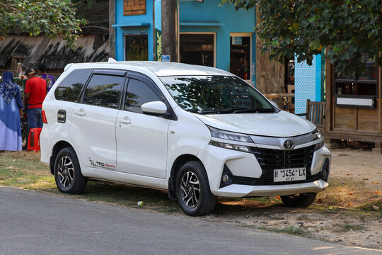 A white Toyota Avanza TRD Sportivo minivan parked on the side of a street near local shops and outdoor activities.