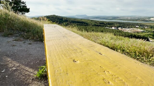 A long yellow bench rests on a scenic grassy hill. It overlooks a distant mountain and a calm reservoir, creating a deeply peaceful and thoughtful feeling.