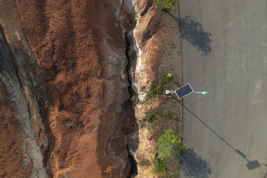 Aerial view of bauxite mining site showing deep red earth excavation, a narrow trench, and a solar-powered street light along a paved road in Indonesia.