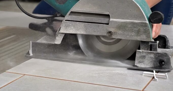 Close up of worker using circular saw to cut ceramic tile flooring installation process.