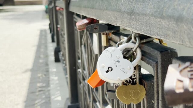 Heart padlocks are locked onto a metal bridge railing next to a walkway. They symbolize eternal romance, joyful commitment, and deep affection shared between couples.