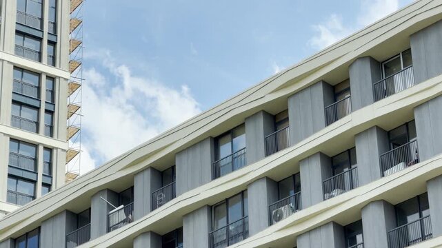 A modern residential building with tiered balconies rises against a clear, sunny sky. The clean architectural lines inspire a feeling of orderly progress and aspiration in the urban environment.