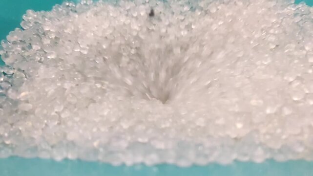 the vortex process of the falling movement of clear polymer plastic granules that pile up from the container for packing