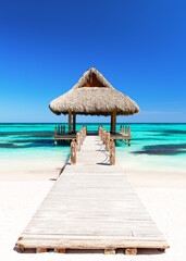 Fototapeta premium Luxury tropical beach scene at Cap Cana in the Dominican Republic featuring a wooden pier, turquoise Caribbean Sea and traditional gazebo.