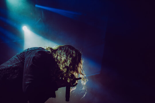Metal singer performing passionately on stage during a club show, with colorful dramatic lighting