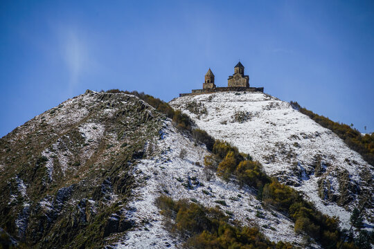 Gergeti Trinity Church Perched on Snowy Mount Kazbegi in Stepantsminda, Georgia Under Blue Sky