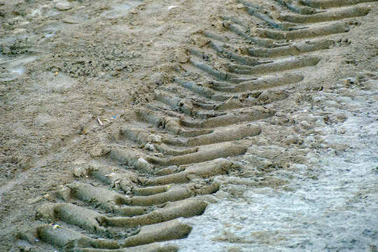Deep heavy tire tracks and aggressive tread marks heavily impressed into the wet gray coastal beach sand signifying human mechanical intrusion into the peaceful natural environment.