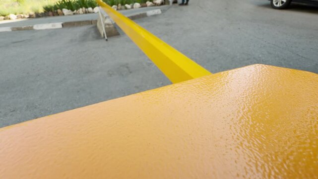 A bright yellow barrier arm blocks the entrance to a quiet parking lot. This industrial gate creates a sense of restriction and patience, standing still under the open sky.